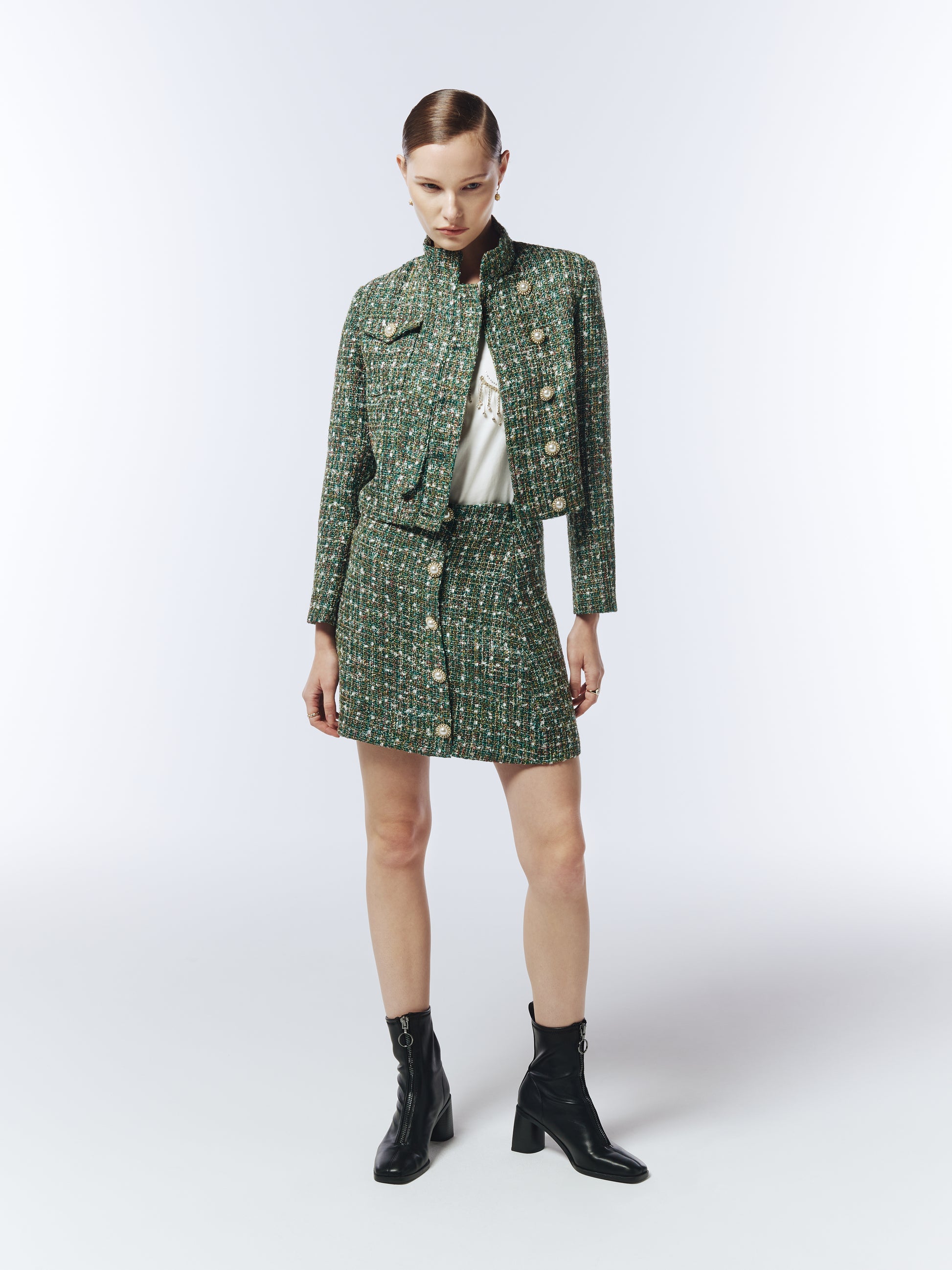 Model wearing SOUR FIGS Cropped High-Neck Tweed Jacket in Emerald Green Mélange with matching mini skirt, showcasing luxury pearl buttons and structured silhouette — perfect for AW25 smart casual and evening looks.