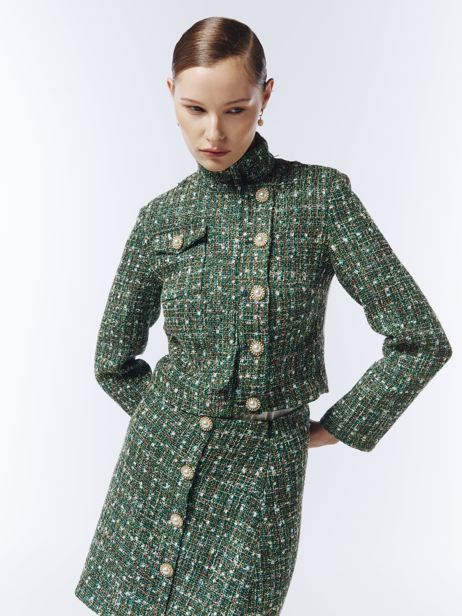 Editorial shot of SOUR FIGS Cropped High-Neck Tweed Jacket in Emerald Green Mélange styled with matching green check tweed skirt, capturing luxury modern tailoring and timeless sophistication.