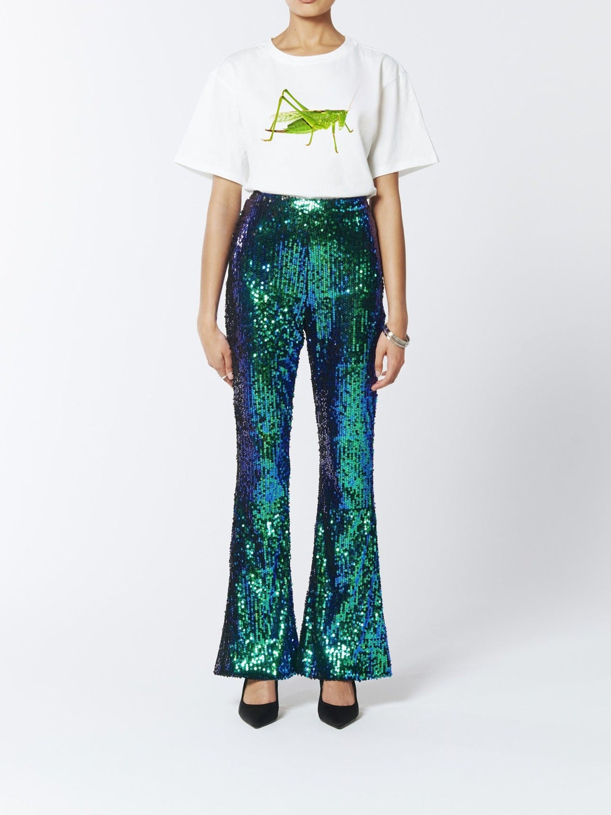 Full-length front view of a model wearing the SOUR FIGS Green Bush-Cricket Print Unisex T-Shirt in White, styled with green and blue sequin trousers and black heels.