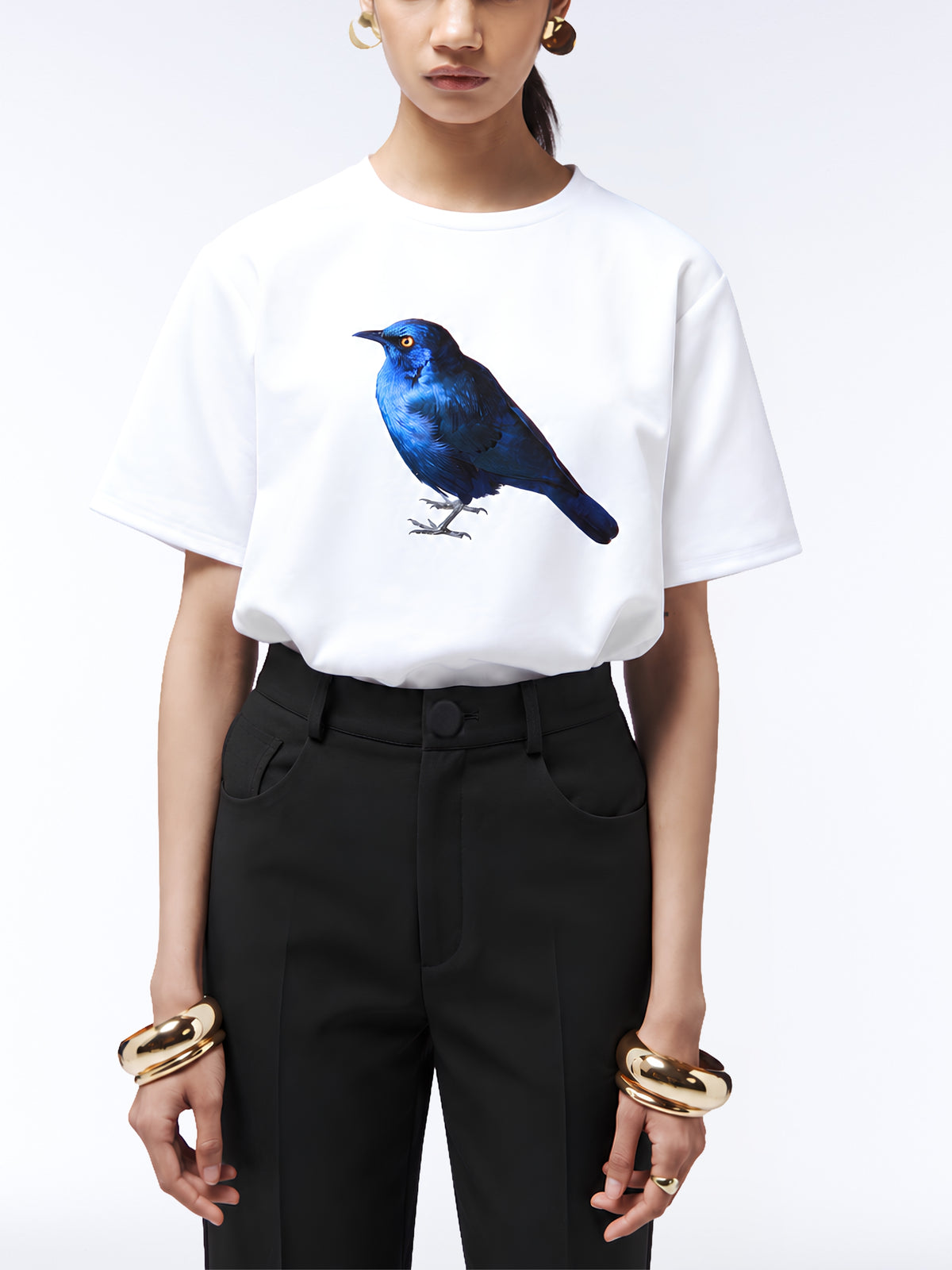 Model wearing the white starling print T-shirt untucked with black trousers, pointed heels and gold jewellery.