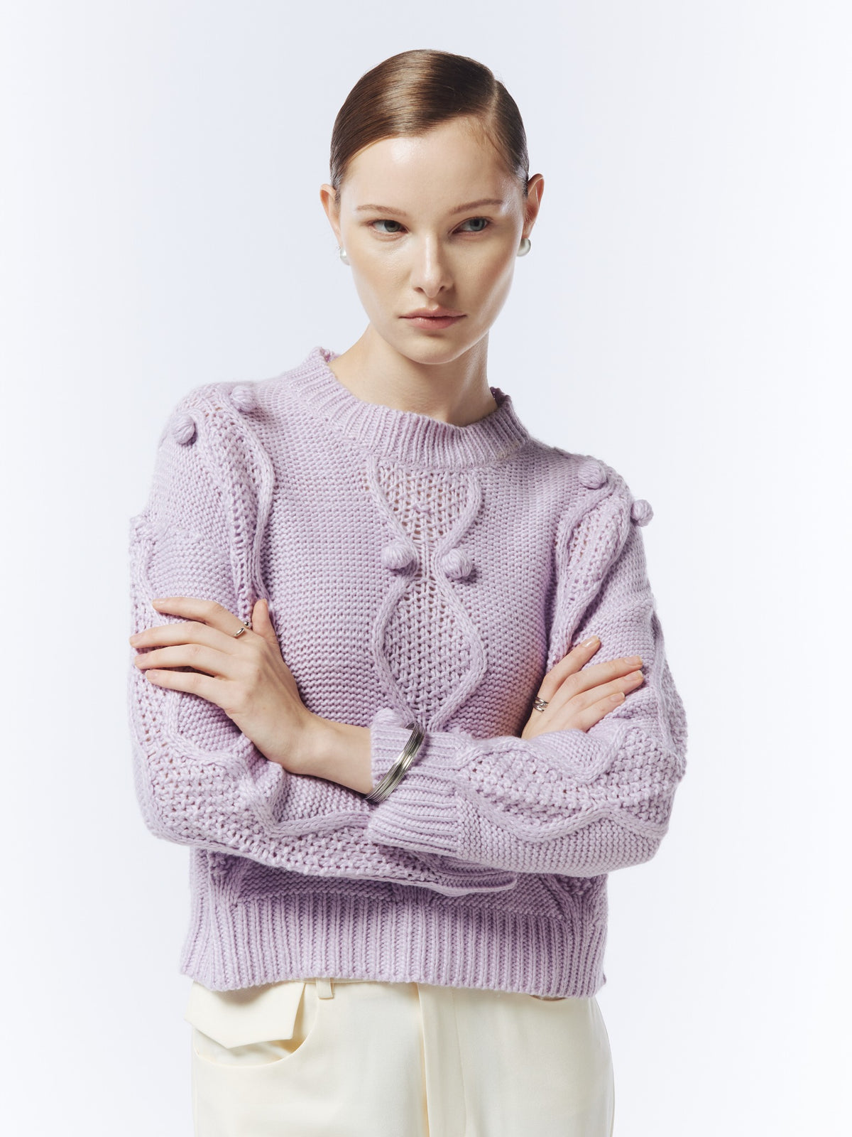Close-up of the soft lilac jumper showing raised bobble details, cable-knit texture and ribbed cuffs.