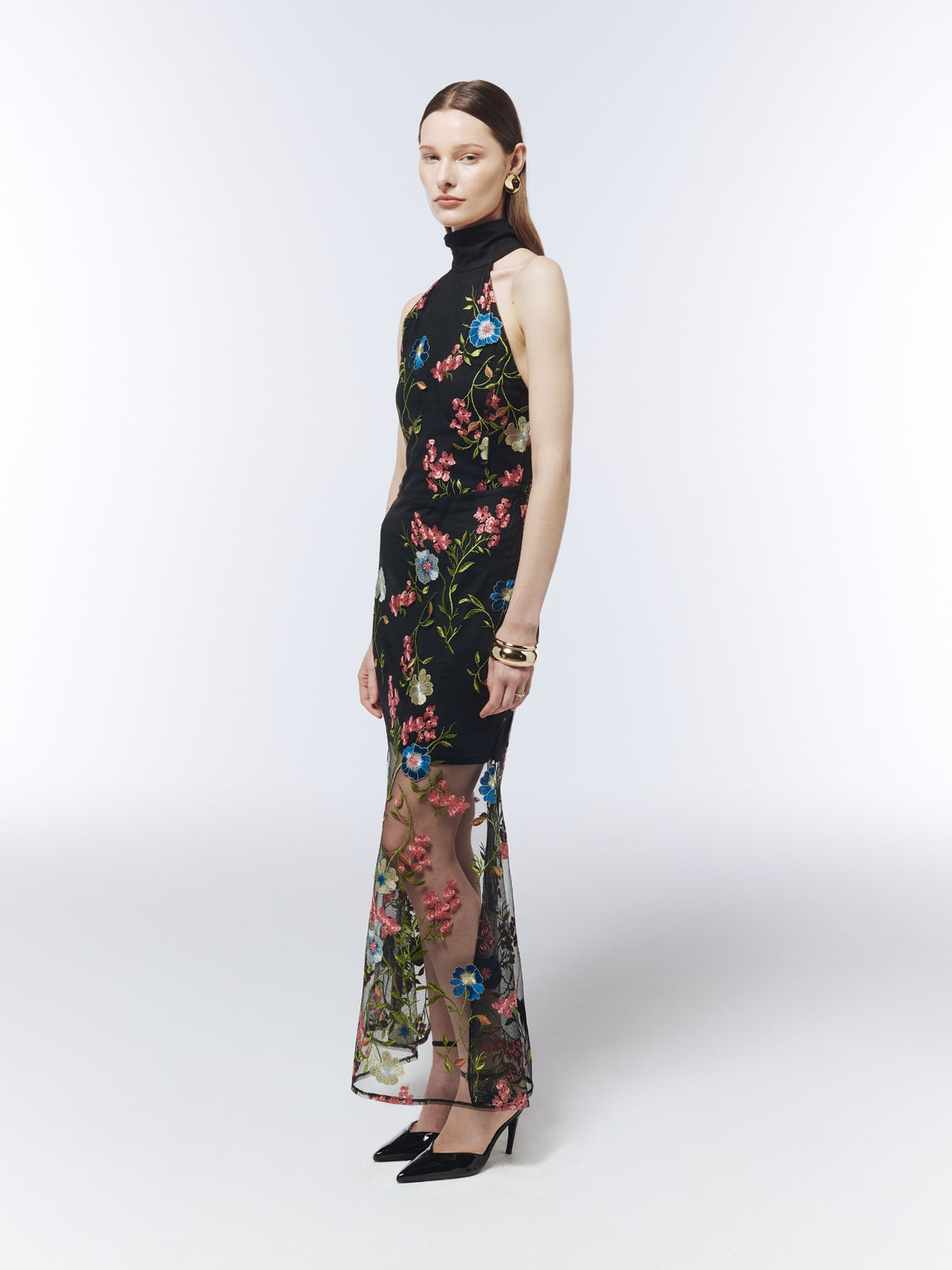 Black floral-embroidered mesh maxi dress, three-quarter model view showing the fitted shape and sheer lower skirt.