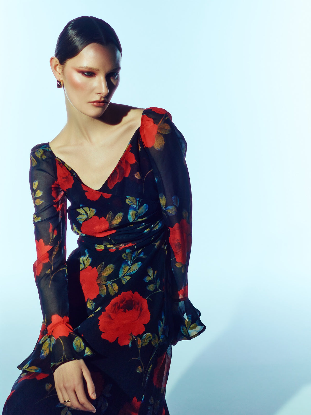 Close-up front model view of the SOUR FIGS Floral Long-Sleeve Maxi Dress in Midnight Rose Black, with red roses, a ruched V-neck bodice and sheer sleeves with flared cuffs.