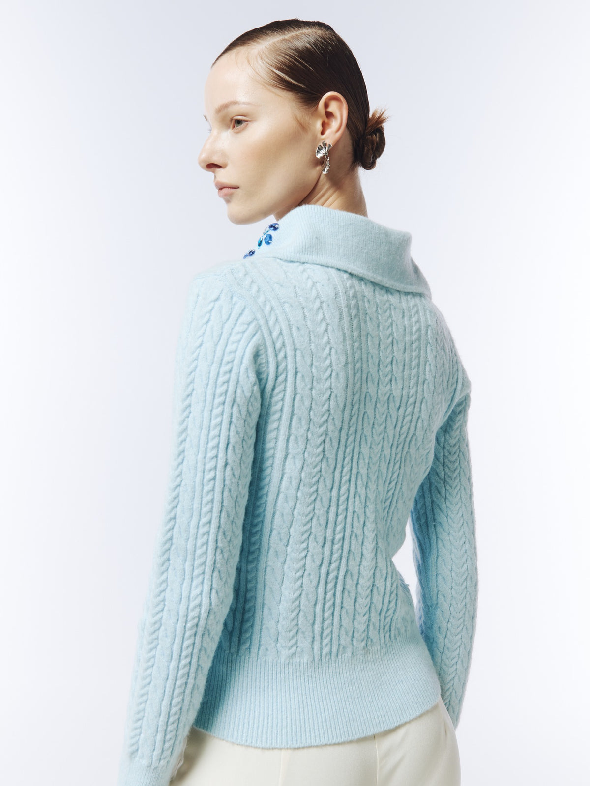 Ice blue hand-embellished cable-knit polo jumper, rear three-quarter model view showing the cable-knit back and ribbed hem.